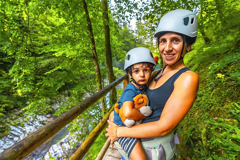 Mother holding her son while wearing helmets and enjoying the stunning view of vintgar gorge near bled, slovenia, creating cherished family memories