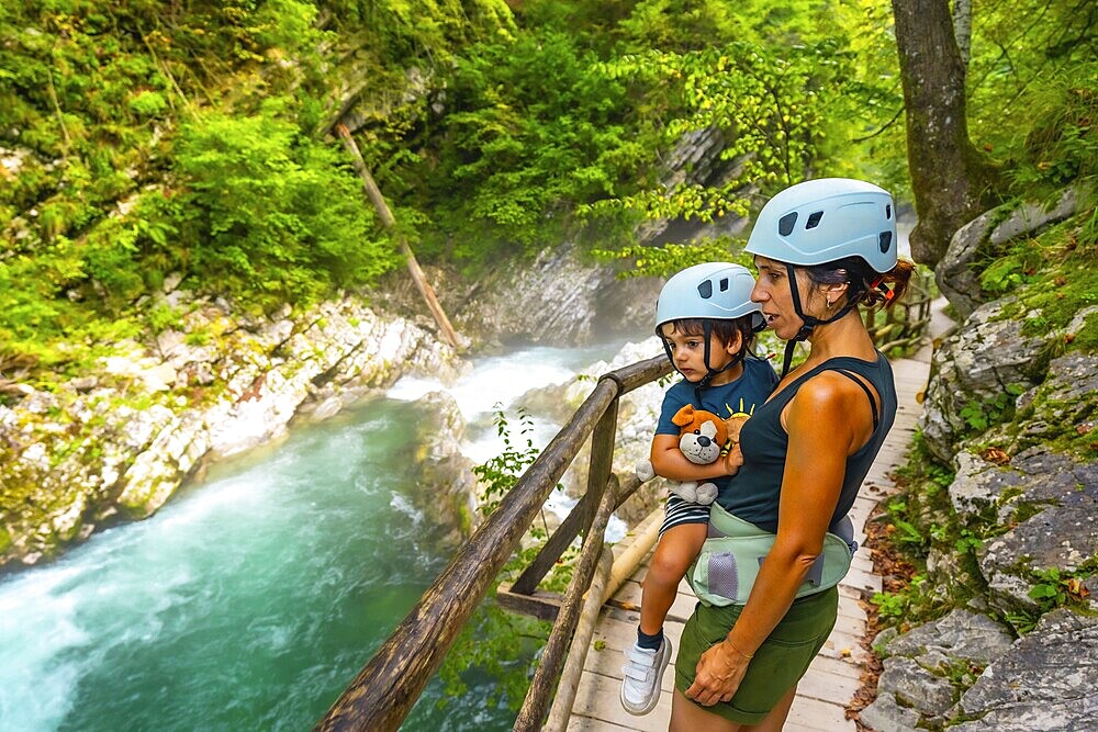 Mother carrying her son while observing stunning turquoise radovna river rapids flowing through vintgar gorge near bled, slovenia