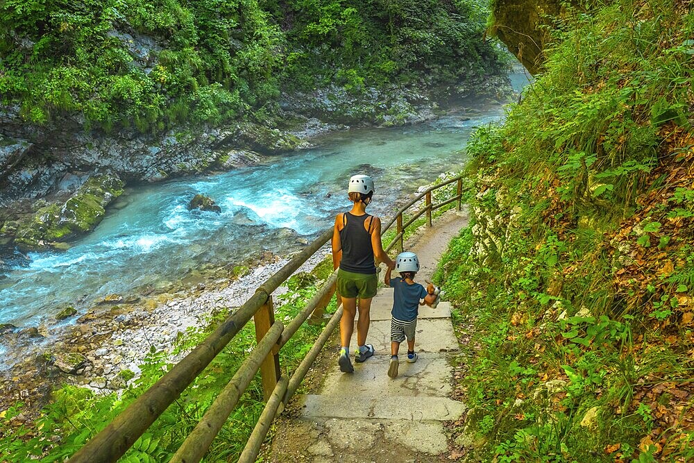 Tourists wearing helmets are enjoying a summer walk along the stunning turquoise radovna river flowing through the vintgar gorge near bled, slovenia