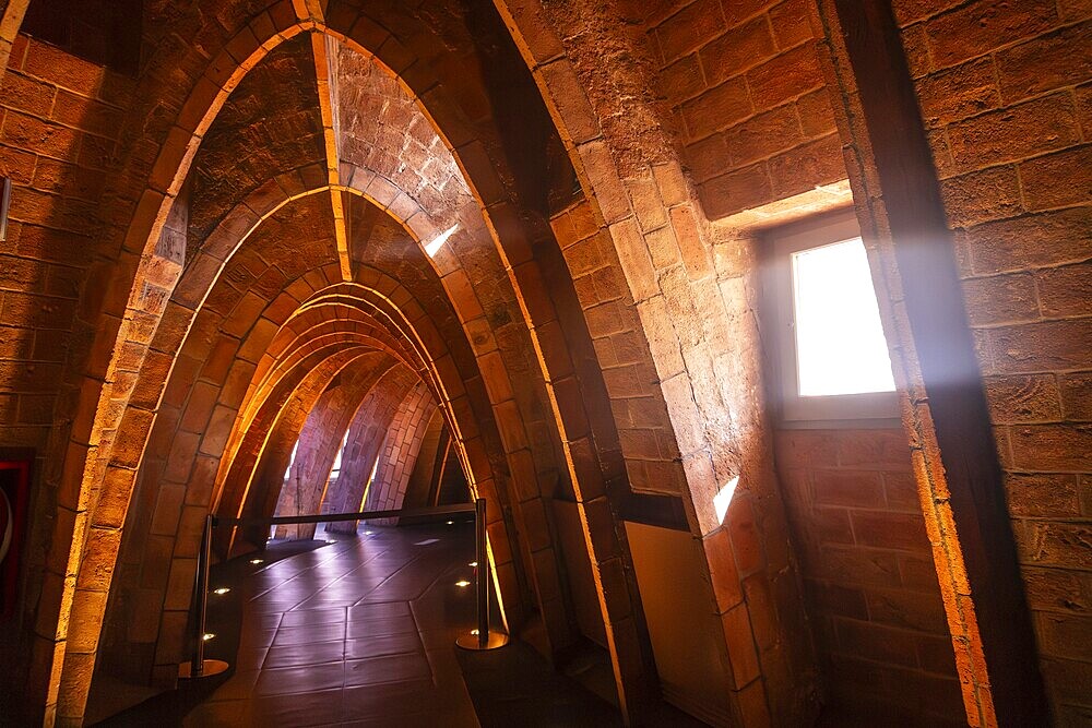 Warm sunlight streams through a window, illuminating the unique brick arches in the attic of casa mila, a famous architectural landmark in barcelona, spain