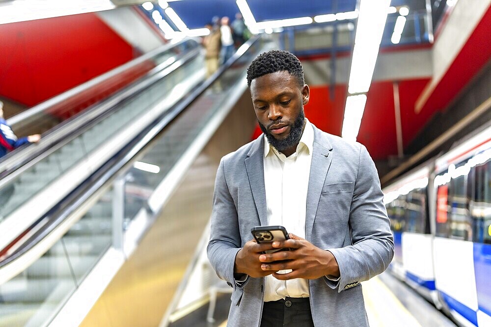 Young businessman waiting for a subway train in a station, using his smartphone to check messages and stay connected while commuting