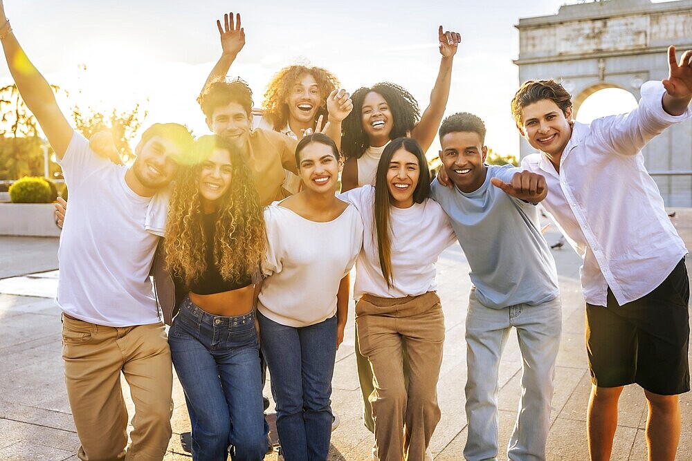 Portrait of diverse group of cheerful young people having fun and raising arms while standing through the city