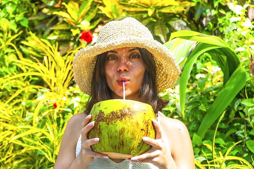 Young woman with straw hat savoring refreshing coconut water, surrounded by vibrant tropical foliage in siargao island, philippines