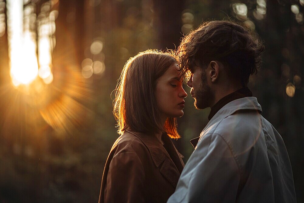 A couple shares an intimate moment in a forest with a sunset glow