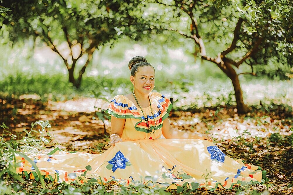 Happy girl in national folk costume sitting on the grass