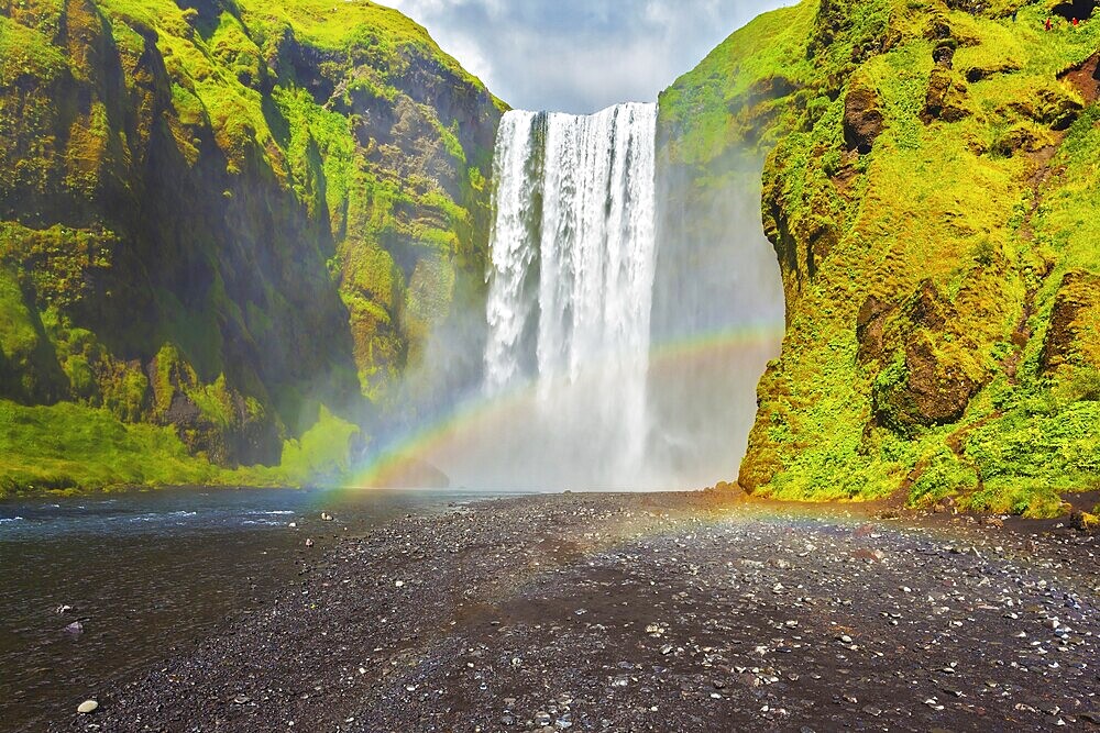 Picturesque huge rainbow appears in the water mist. The most popular waterfall in Iceland - Skogafoss. Water rushes down with a crash, forming a cloud of mist
