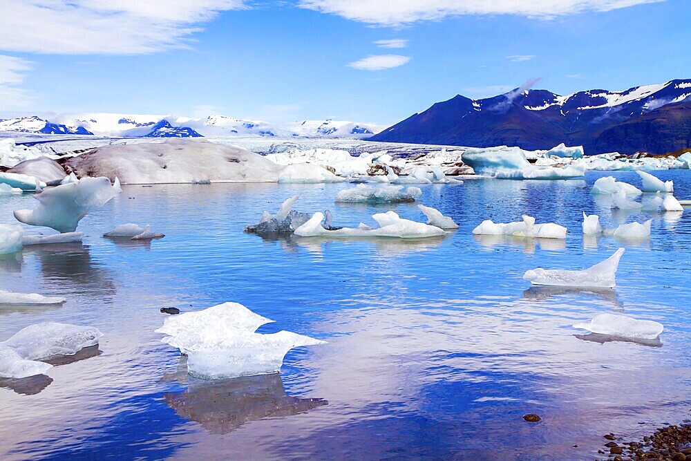 Cold, clear July day. Bizarre icebergs and floating ice floes reflected in the smooth cold water of the lagoon. The lagoon Jokulsaurloun. Iceland. The concept of eco, northern and photo tourism