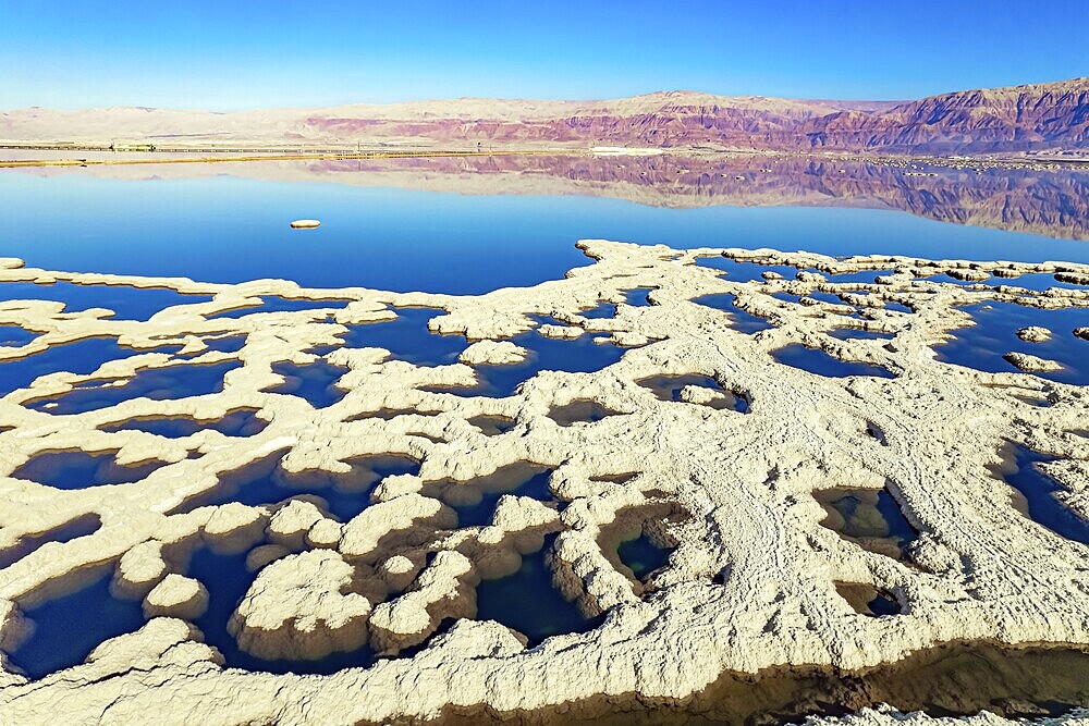 Dead Sea. Evaporated salt forms bizarre patterns on the water. Sunny winter day. The blue water is surrounded by pink mountains. The picture was taken by a drone from a aerial view. Israel