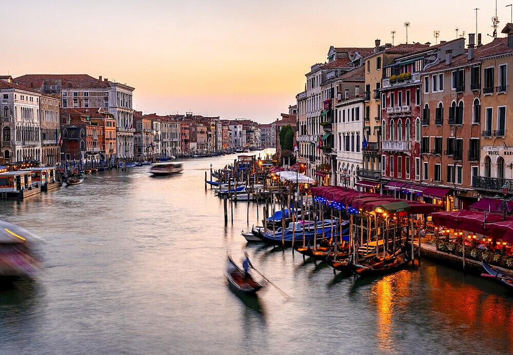 View of the Grand Canal with gondoliers at sunset, picturesque evening mood with illuminated palazzos on the canal, long exposure, view from the Rialto Bridge, Venice, Veneto, Italy, Europe