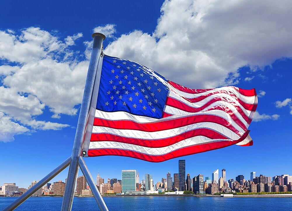The skyline of Manhattan shines brightly over the East River with a flag