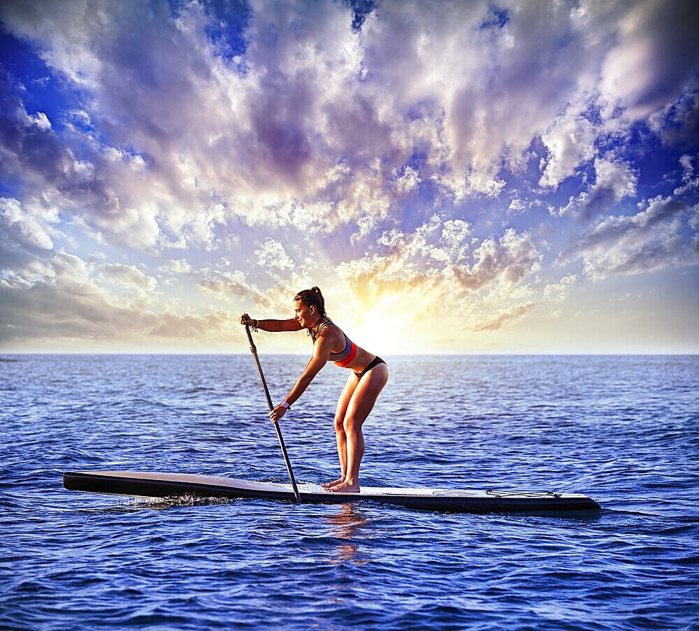 SUP Stand up Surf girl with paddle in a blue ocean sea