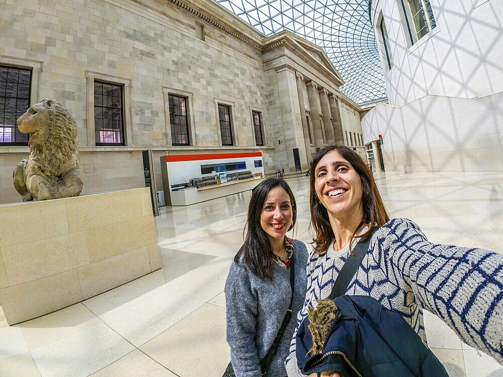 Two happy female tourists are taking a selfie with a fisheye lens at the british museum's great court in london, uk