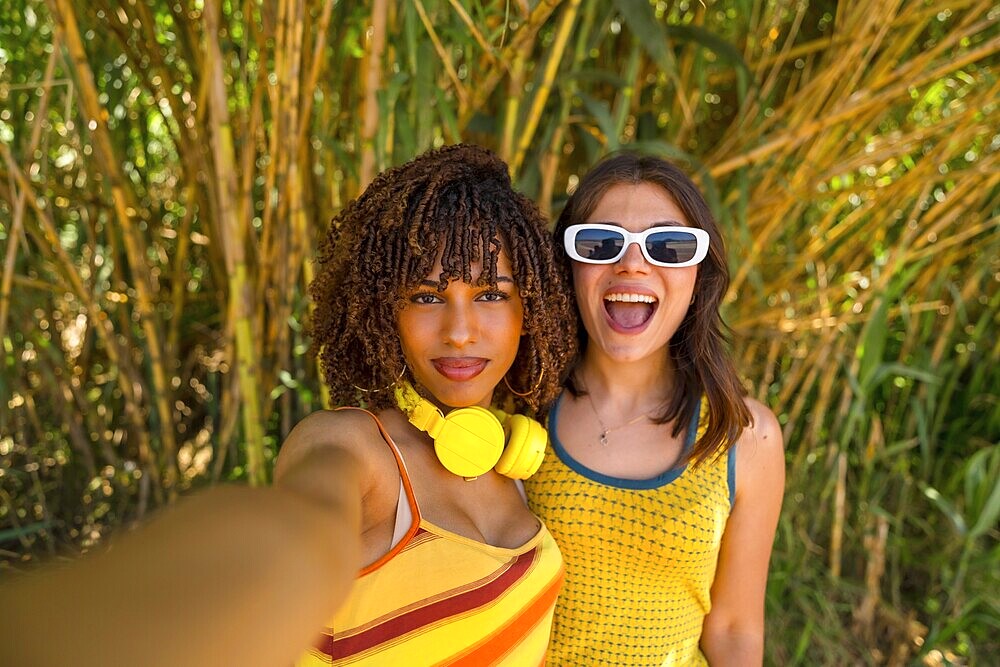 Two cheerful female friends capturing a joyful selfie while enjoying their vacation in a lush bamboo forest, surrounded by vibrant greenery