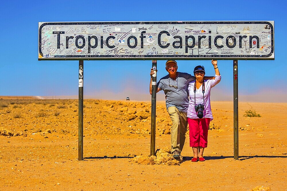 Happy elderly couple of tourists. South Tropic, or Tropic of Capricorn, - the famous road sign in Namibia. The concept of extreme and active tourism