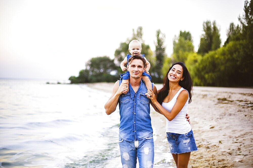 Beautiful young family on holiday with baby. The father holds the blonde girl in her arms, and the brunette's mother hugs her husband. The concept of a family beach holiday summer near the sea