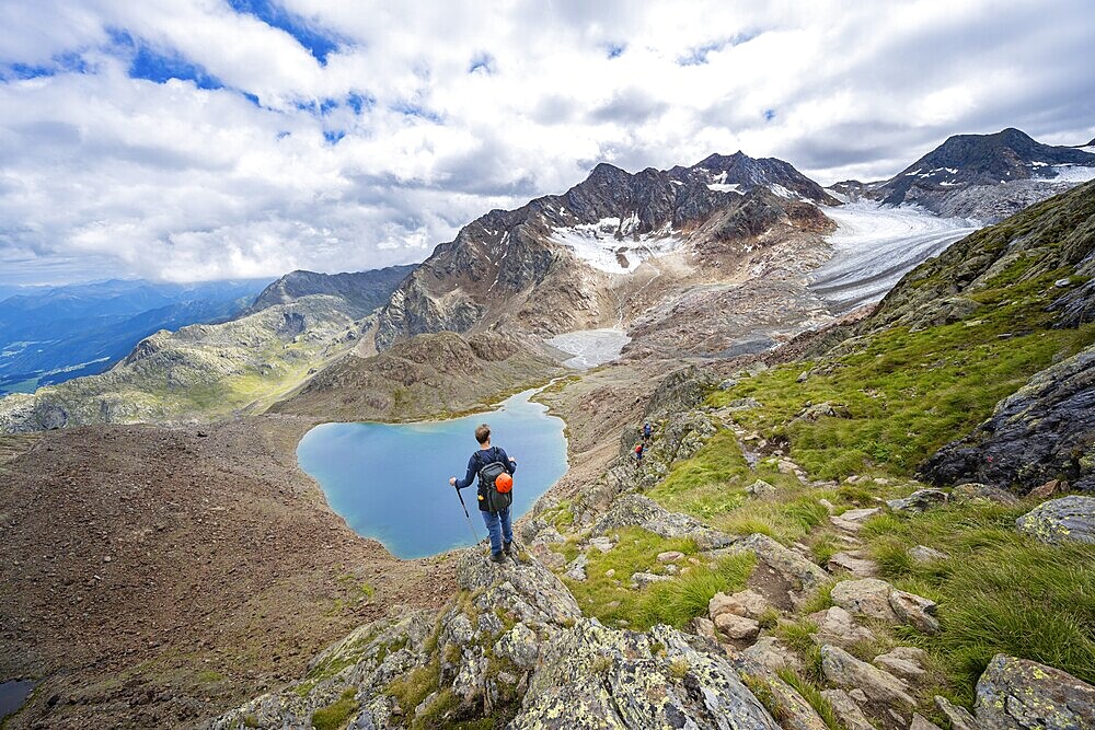 Mountaineer in front of dramatic high mountain landscape, view of mountain lake Vogelhüttensee and glacier Übeltalferner, Stubai Alps, South Tyrol, Italy