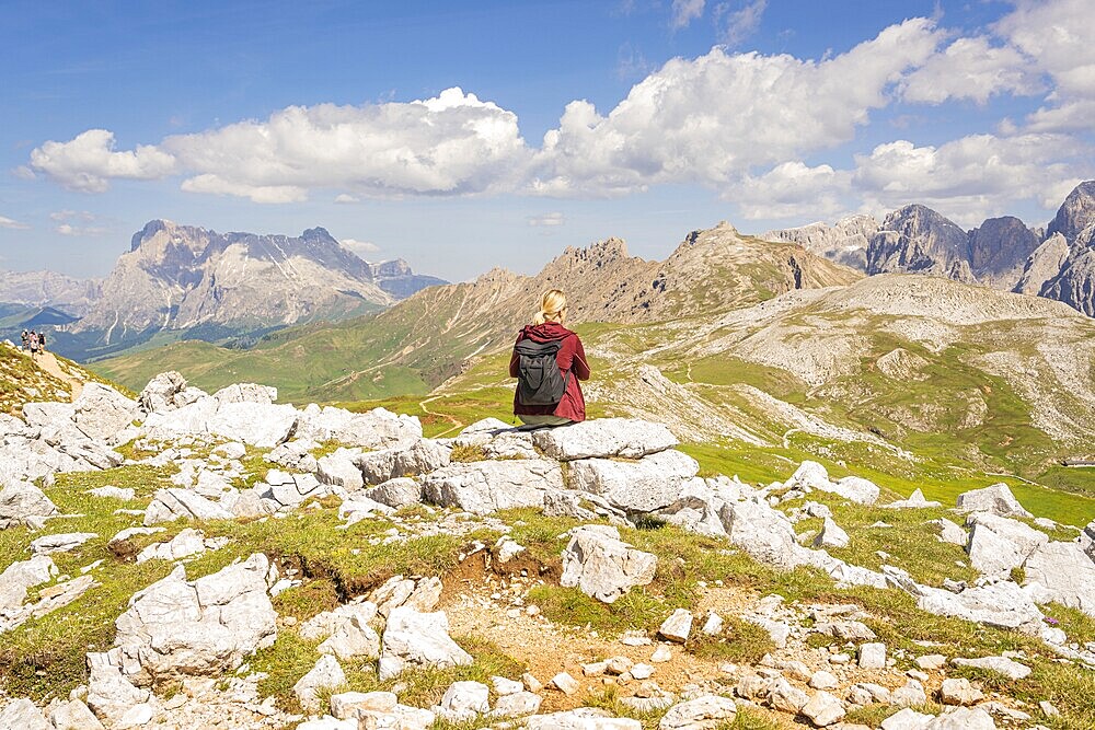 Person sitting on rock with rucksack, mountain panorama and blue sky in the background, hike to Schlehrn, Alpe di Siusi, Dolomites, South Tyrol, Italy