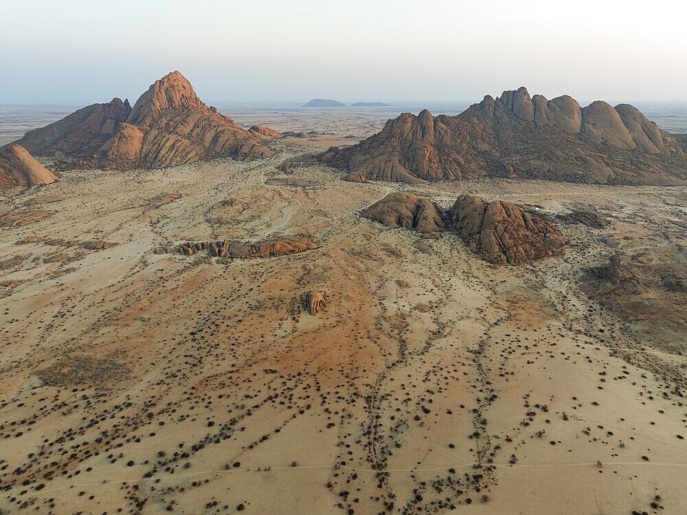 Spitzkoppe (1728 m) - on the left - and Pondok Mountain majestically rise above the surrounding desert plains. At dawn. Aerial view. Drone shot. Damaraland, Namibia
