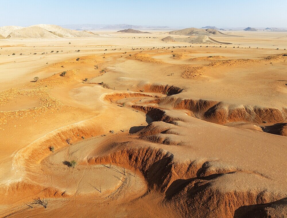 Canyons, arid plains grown with camelthorn trees (Vachellia erioloba) and isolated mountain ridges in the Tsondab Valley in the Namib Desert. Aerial view. Drone shot. Namibia