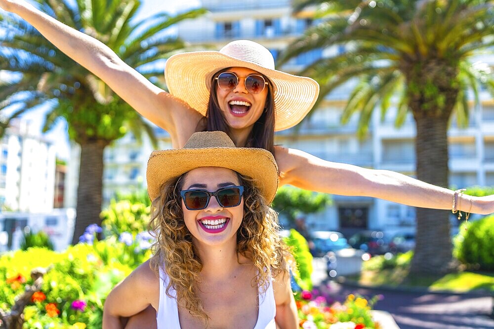 Two cheerful female friends are having fun during summer vacation, wearing sunglasses and straw hats