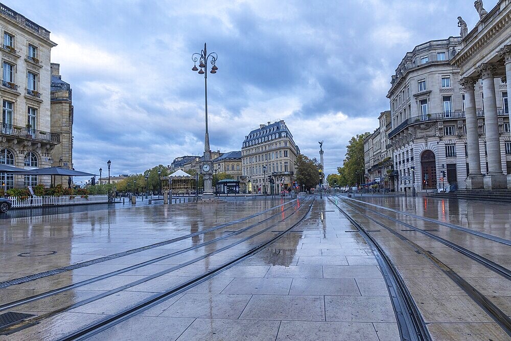 Comedie square in bordeaux city centre with wet tram tracks reflecting surrounding buildings on a cloudy morning
