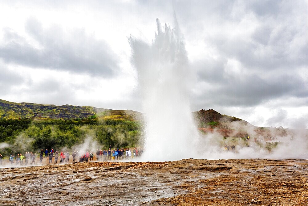 Active Strokkur, tourists observe eruption, high temperature area Haukadalur, tourist attraction at the Golden Circle, Sudurland, Iceland