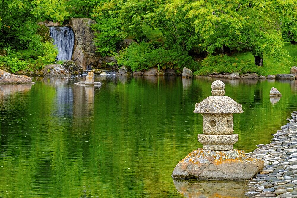 A waterfall and a stone lantern next to a tranquil pond in the Nikka Yuko Japanese Garden in Lethbridge, Alberta, Canada