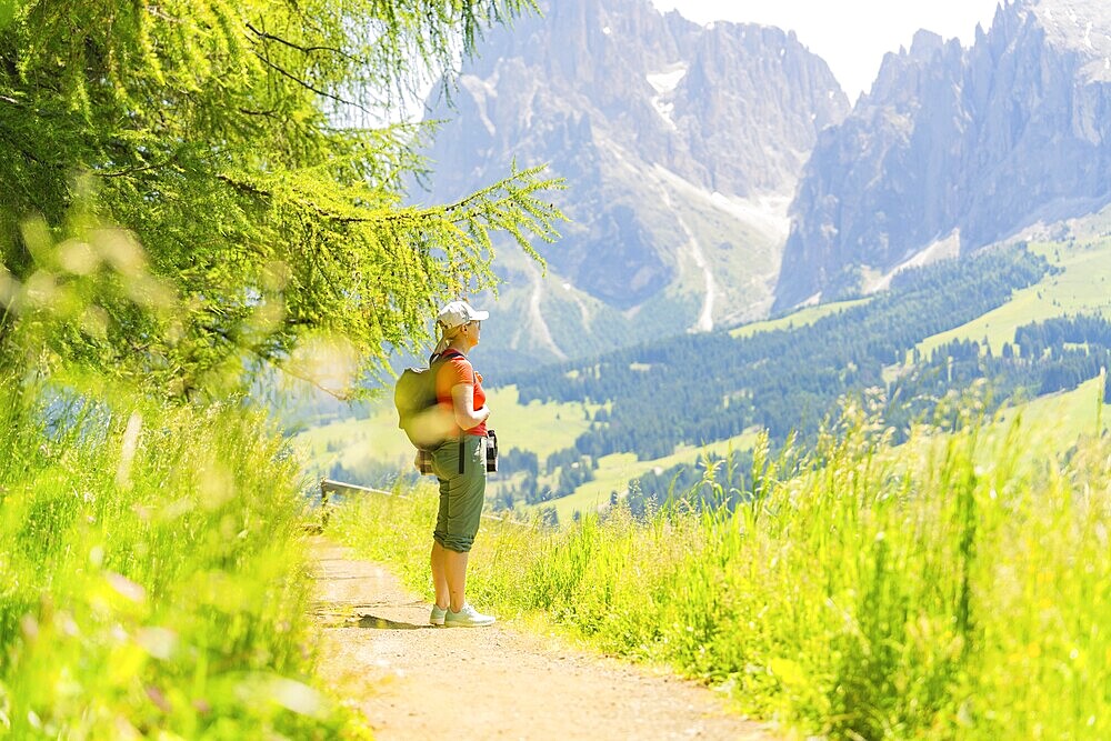 Person walking on a path with a view of mountains on a sunny day, Alpe di Siusi, Dolomites, South Tyrol, Italy