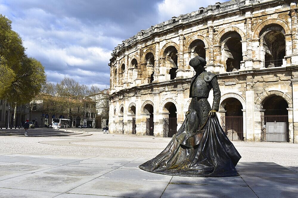 Statue in front of a historic Roman amphitheater under a cloudy sky. Herault, France
