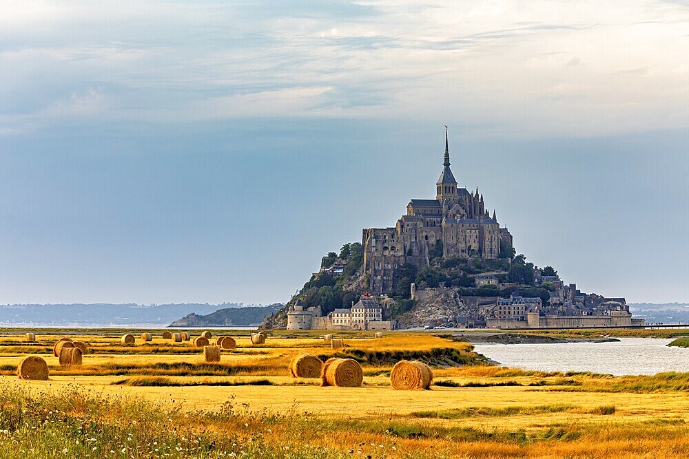 A historic castle under a cloudy evening sky surrounded by fields, Mont Saint Michel in Normandy, France