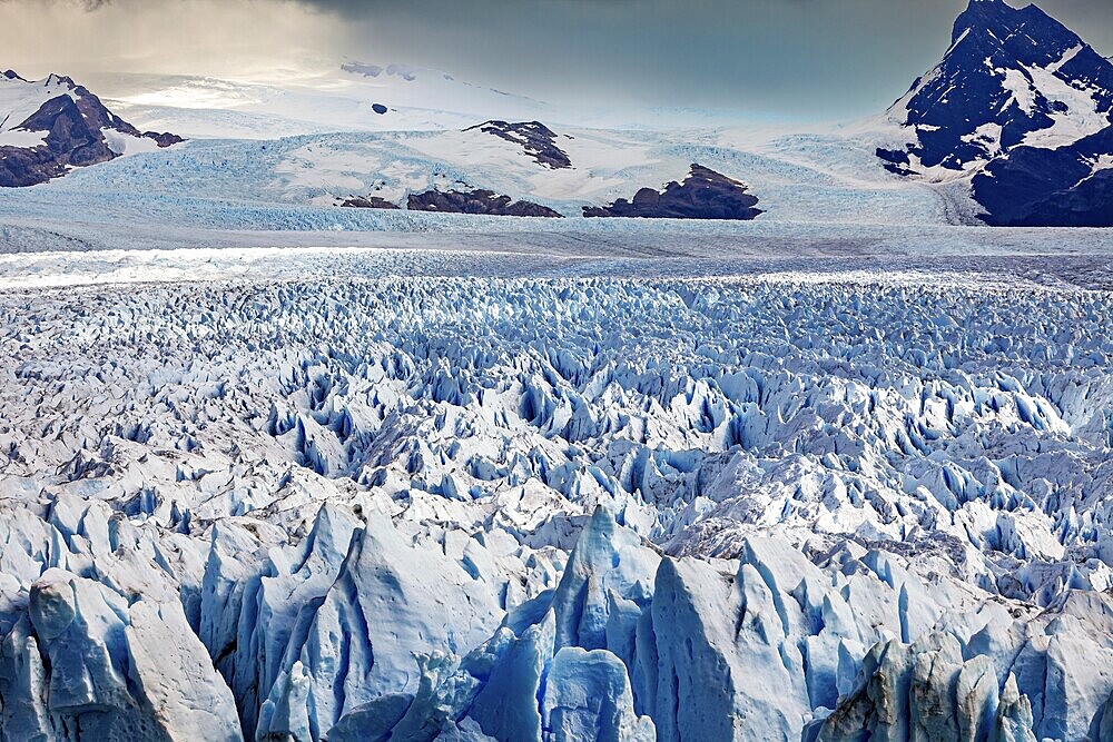 A vast icy landscape stretches out in front of a cloudy sky and majestic mountain peaks, The Perito Moreno glacier in Argentina