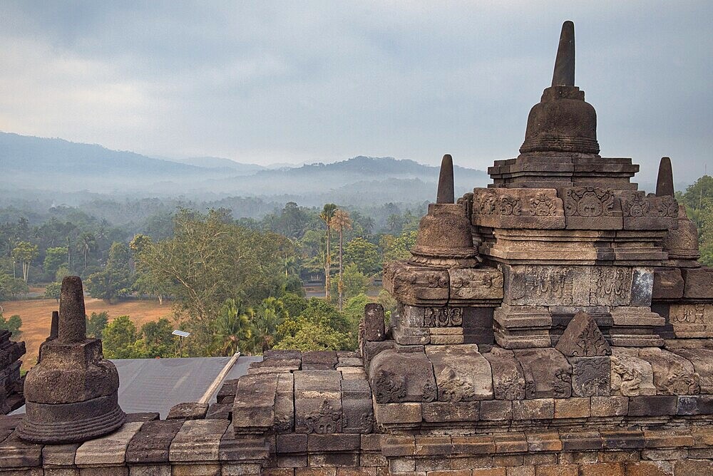 Stone temple structures with a forested mountain landscape in the background, Candi Borobudur, Borobudur, Java, Indonesia