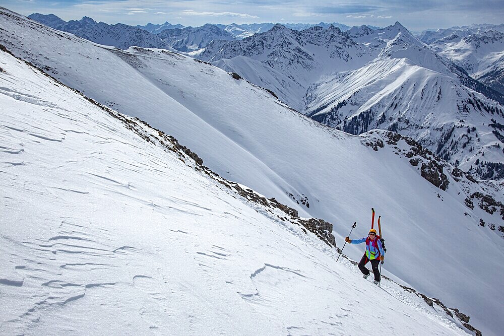 A ski tourer ascending a very steep summit slope, ski tour to the Thaneller, in the background the snow-covered high mountain landscape of the Lechtal Alps, Tyrol, Austria