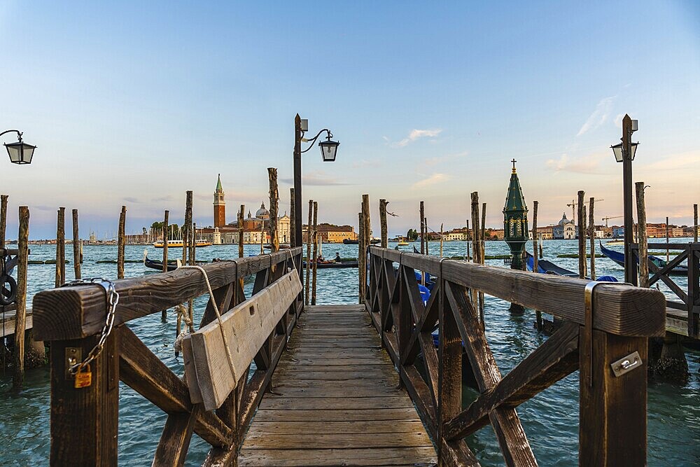 Wooden pier with gondolas and lamps leading to san giorgio maggiore in venice at sunset, creating a romantic and picturesque view