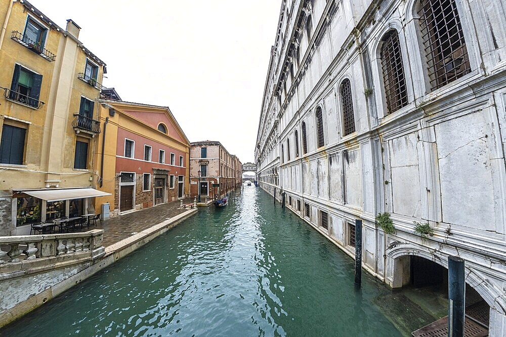 Serene canal in venice with traditional gondola navigating towards distant bridge, showcasing colorful buildings and historic architecture