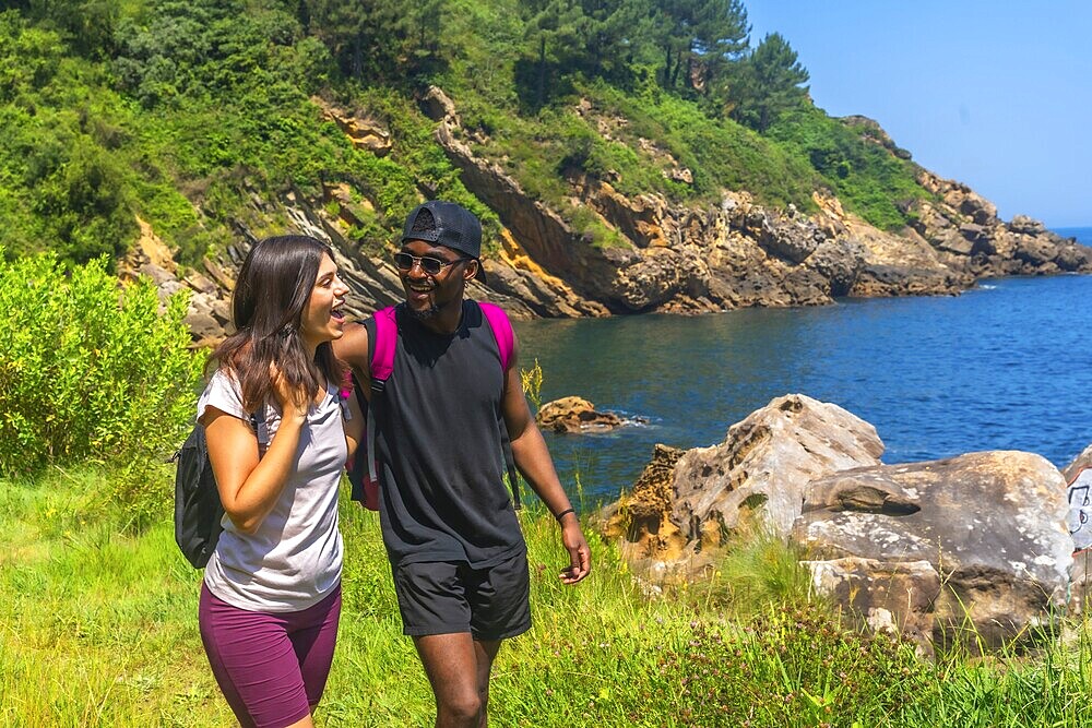 Young couple walking and laughing along a beautiful coastline path on a sunny summer day, enjoying the scenic views
