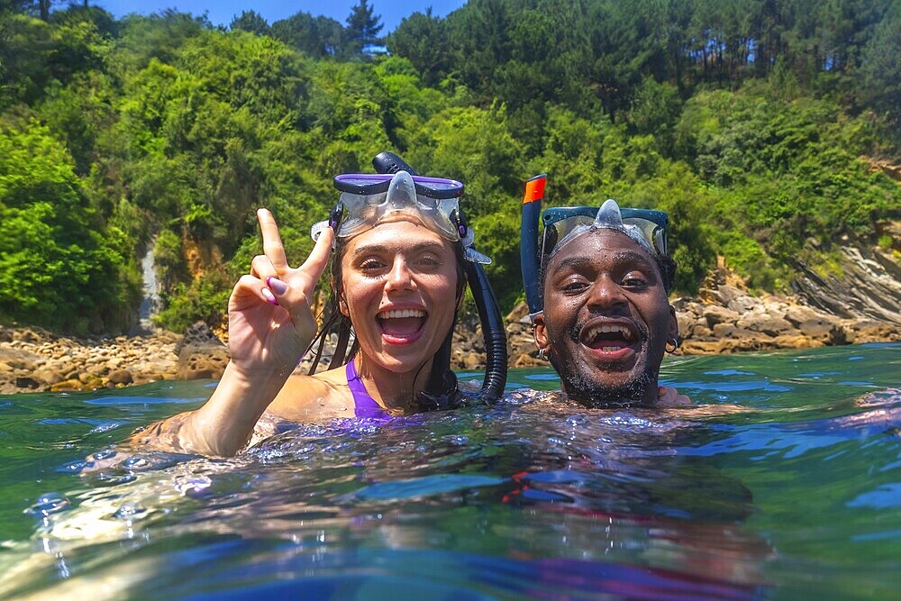 Young multi ethnic couple enjoying snorkeling together in crystal clear tropical sea, woman making victory sign
