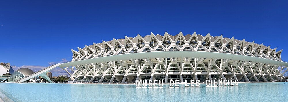 Panoramic photo Futuristic, unique and spectacular modern architectural building science museum Prinz Philip (Museu de les Ciències) with large text MUSEU DE LES CIENCIES, with blue sky in the background on the water in the ultra-modern science complex in a landscaped park Ciudad de las Artes y de las Ciencias, Quatre Carreres, Valencia, Autonomous Community of Valencia, Province of Valencia, Spain