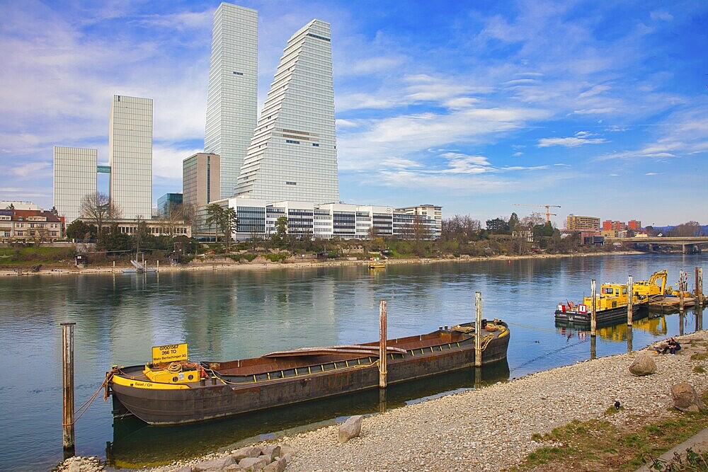 A cargo ship lies on the riverbank in Basel with modern skyscrapers in the background, pharmaceutical company Roche, skyscrapers, towers, Rhine, Basel, Switzerland