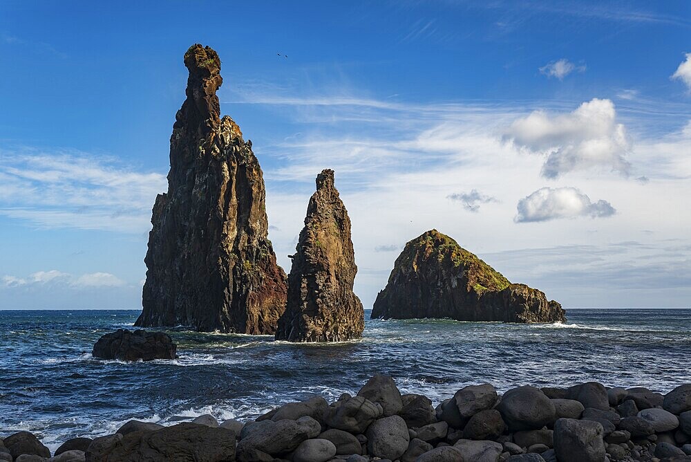 Dramatic rock formations rise out of the sea on the rocky beach of Ribeira da Janela, surrounded by sky, Madeira, Portugal