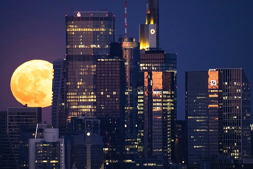 The full moon passes behind the Frankfurt banking skyline, Frankfurt am Main, Hesse, Germany