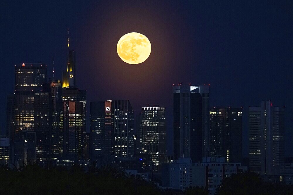 The full moon passes behind the Frankfurt banking skyline, Frankfurt am Main, Hesse, Germany