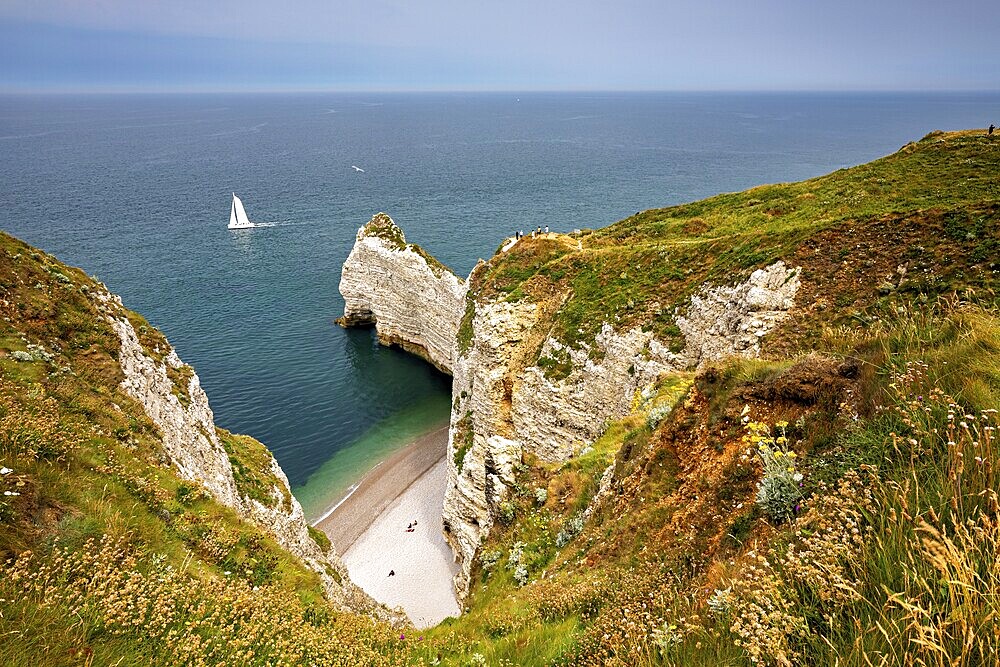 Green cliffs with sailing boat in the sea and small beach bay, The cliffs and alabaster coast of Etretat in Normandy France