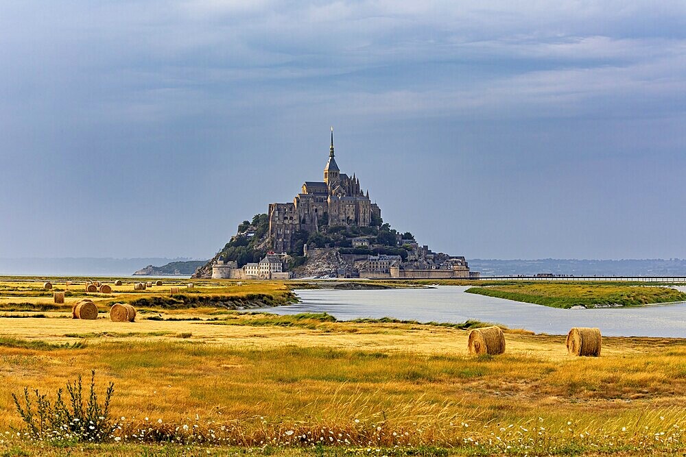A castle island with ecclesiastical architecture in a rural landscape under a cloudy sky, Mont Saint Michel in Normandy, France