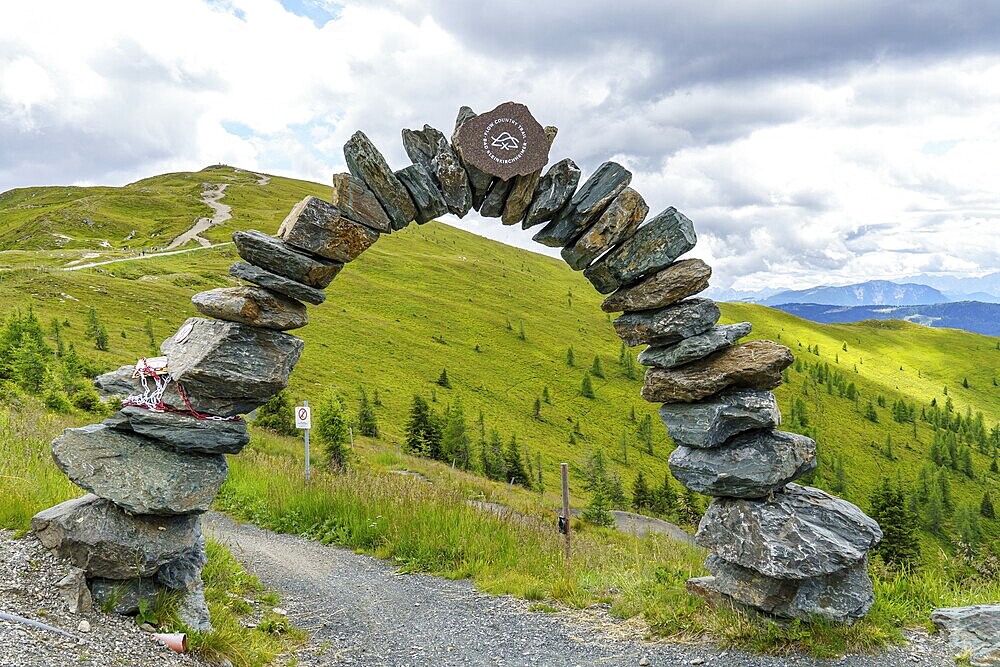 Stone arch on a hiking trail with a view of green hills and cloudy sky, Bad Kleinkirchheim, Carinthia, Alps, Austria