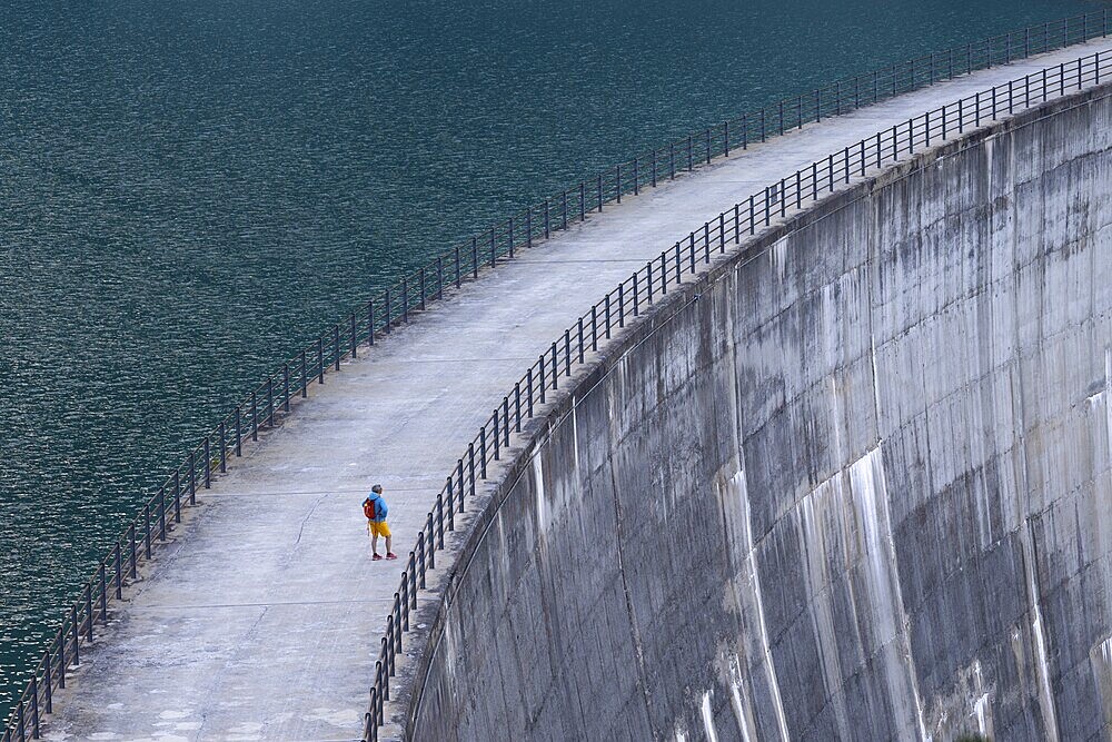 Woman, walking alone along a large dam with a view of the endless expanse of water, Zervreilastausee, Vals, Canton Graubünden, Switzerland