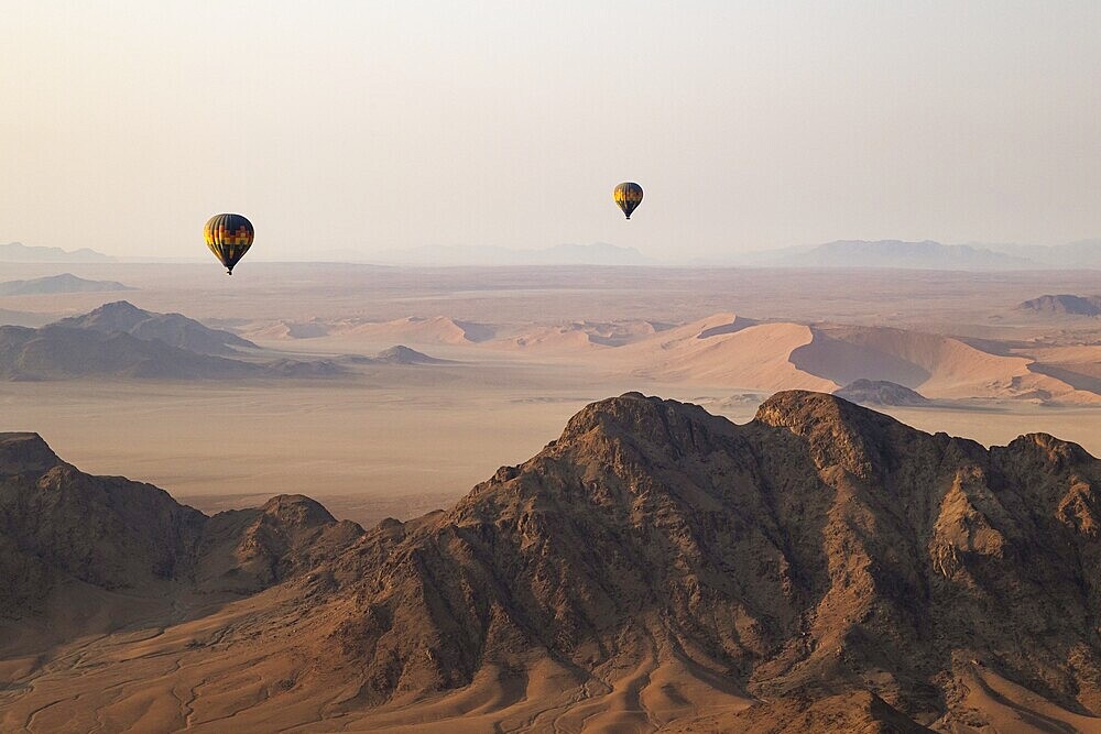 Two hot-air balloons above an arid plain and isolated mountain ridges at the edge of the Namib Desert. Aerial view from another balloon. Namibia