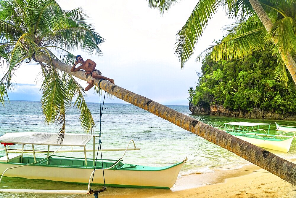 Young man relaxing on a palm tree over a tropical beach in kangbangyo island, siargao, philippines