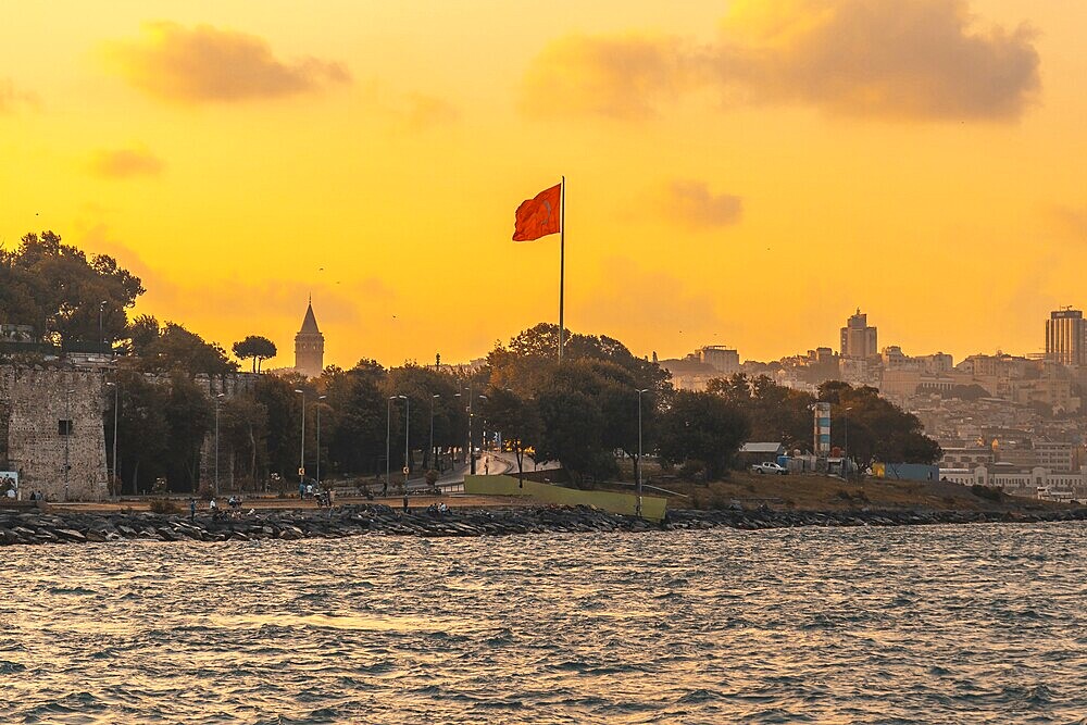 Scenic sunset view of istanbul's cityscape, featuring the prominent galata tower and a waving turkish flag, creating a patriotic and picturesque scene