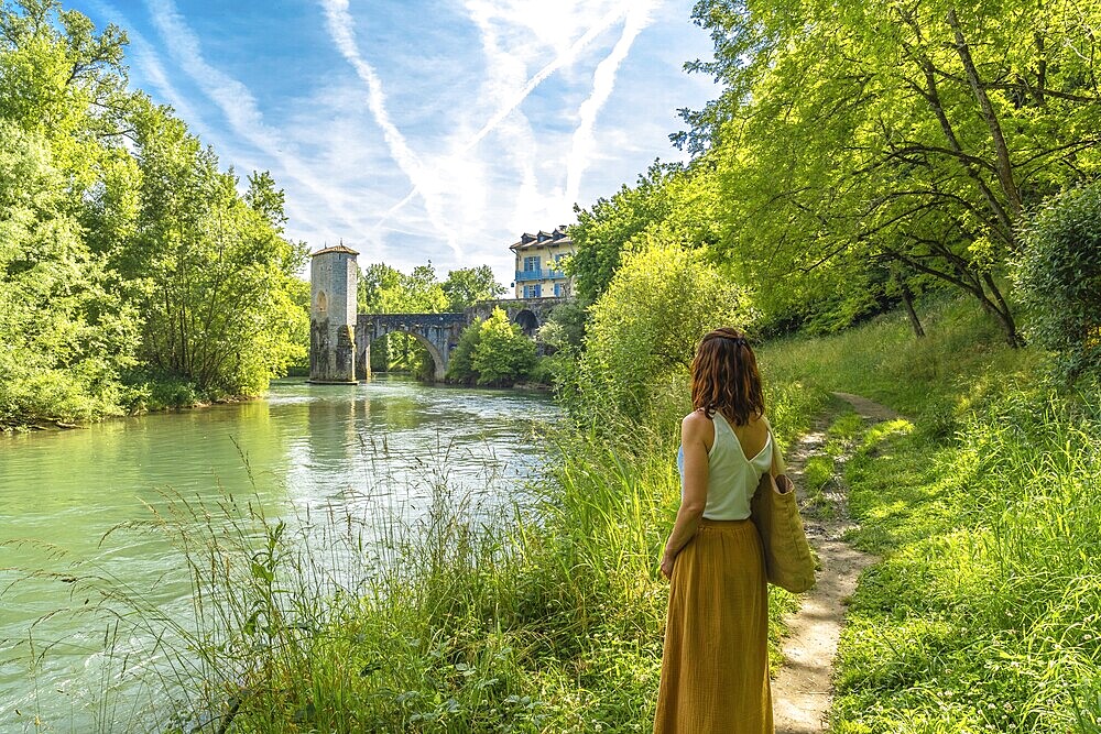 Woman enjoying summer vacations in french countryside admiring the medieval bridge and tower of sauveterre de bearn in the pyrenees atlantiques